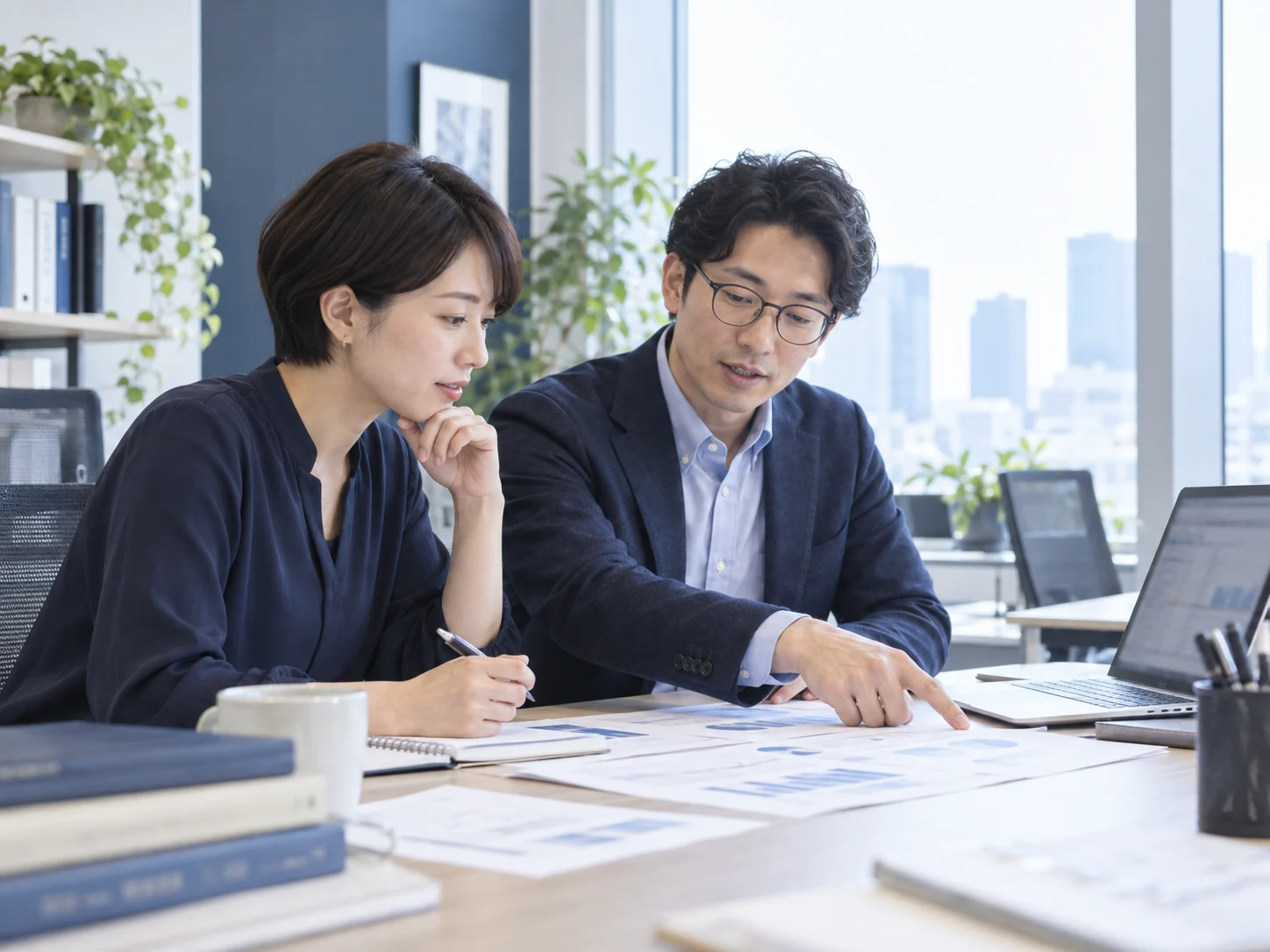 帳票とパソコンで需要計画を確認する二人の担当者