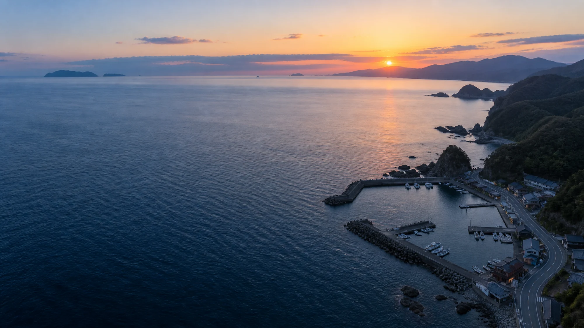 夕暮れの海と漁港の空撮