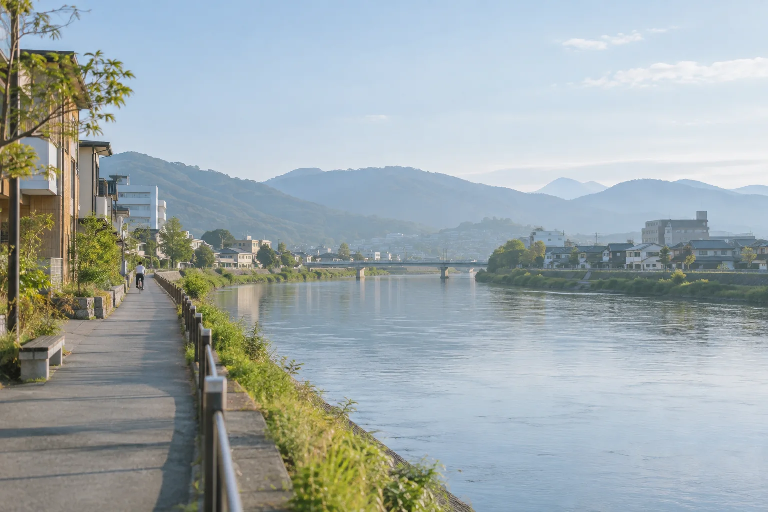 川沿いに低い建物が並び、遠くに山並みが見える地方都市の朝